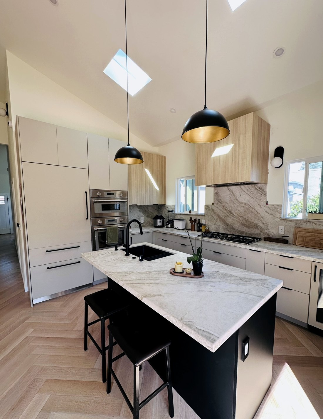 Kitchen under a vaulted ceiling with a skylight, oak casework, stone counters, and herringbone oak floor