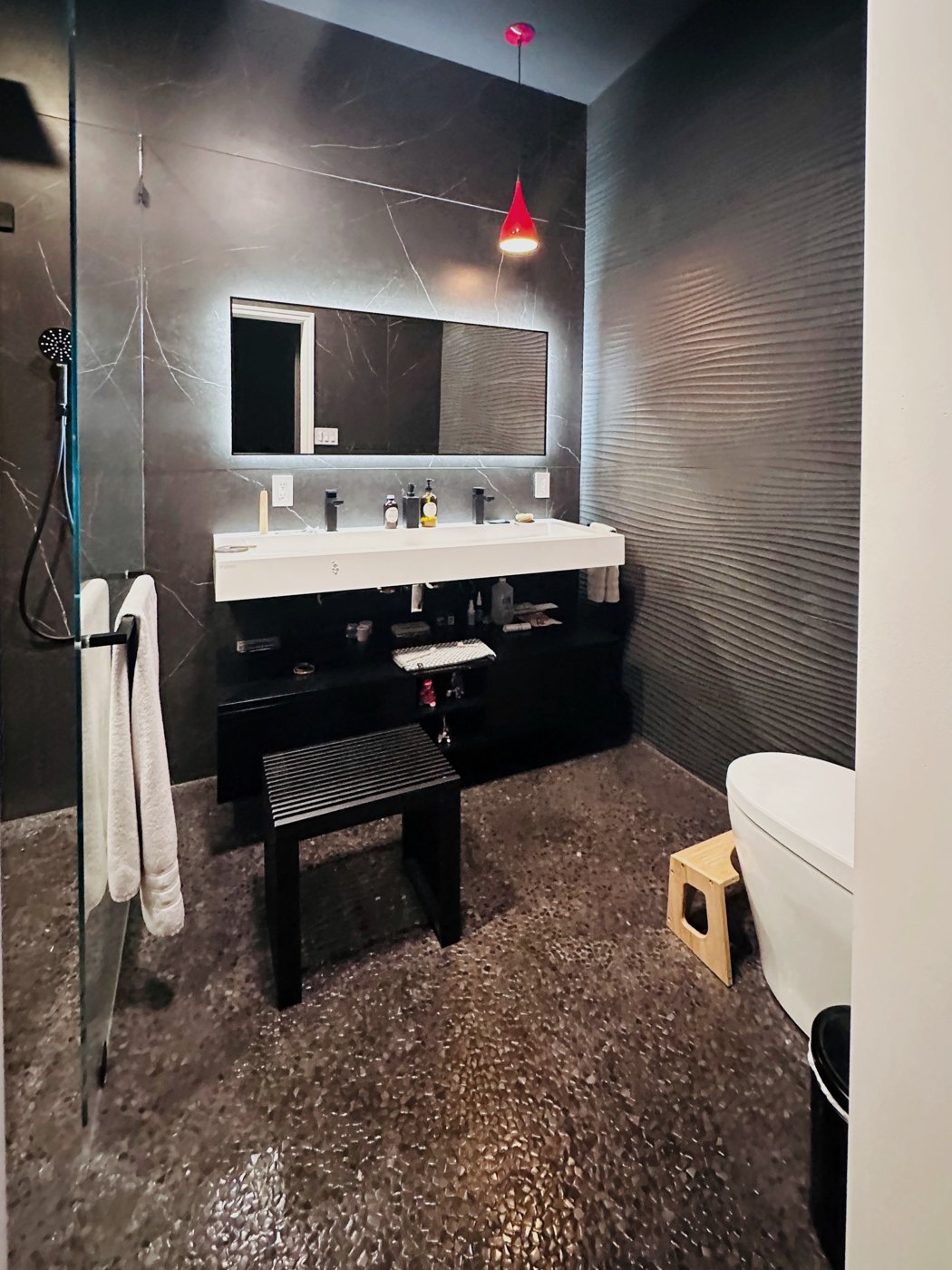 Primary bath with dark porcelain panels and a pebble mosaic floor