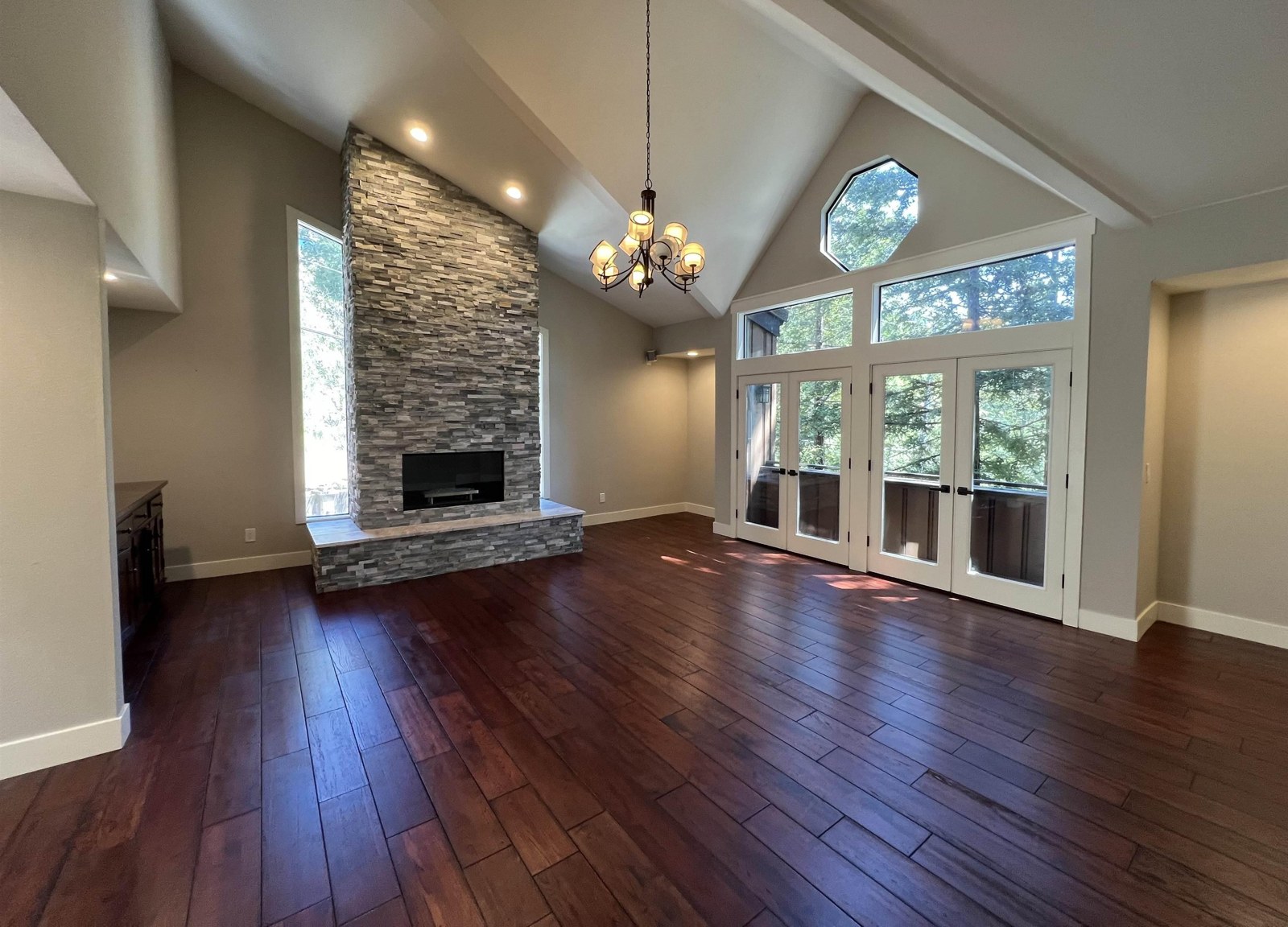 The great room before, with dark floors and a stacked-stone fireplace